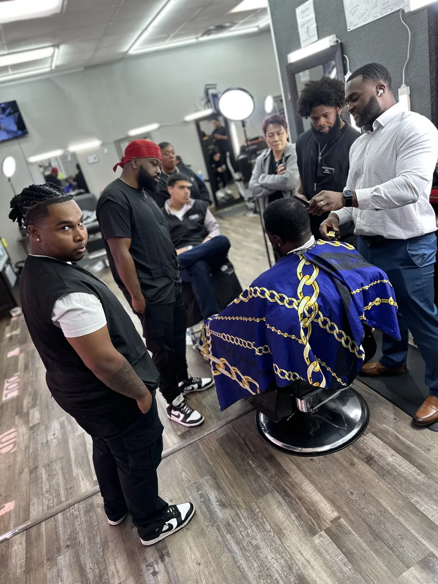 Students gather around a chair while an instructor works on a client in a blue cape